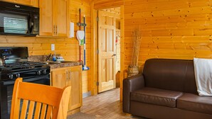 A wooden cabin interior with a kitchen area, a brown leather sofa, and a wooden chair. - Long Beach RV & Camping Resort (Ilwaco)