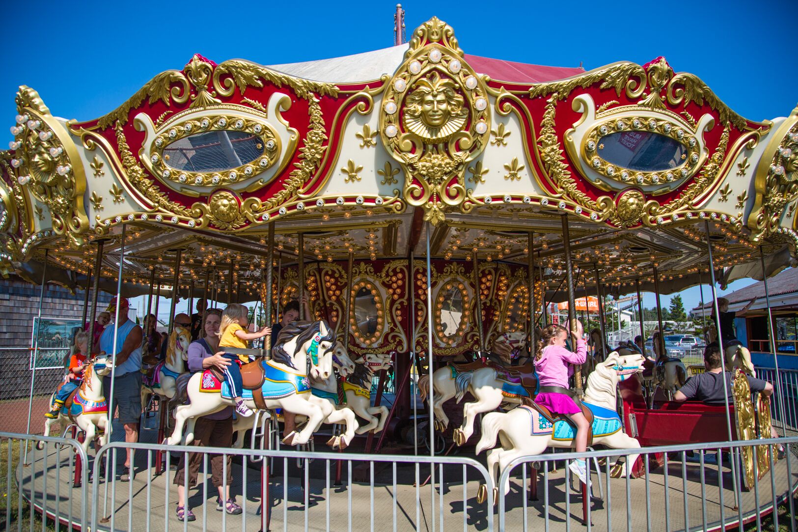 A carousel with ornate golden and red decorations, featuring horses with riders.