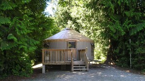 A small, single-story cabin with a wooden deck and a covered porch, surrounded by dense forest. - Mount Vernon RV Campground (Bow)