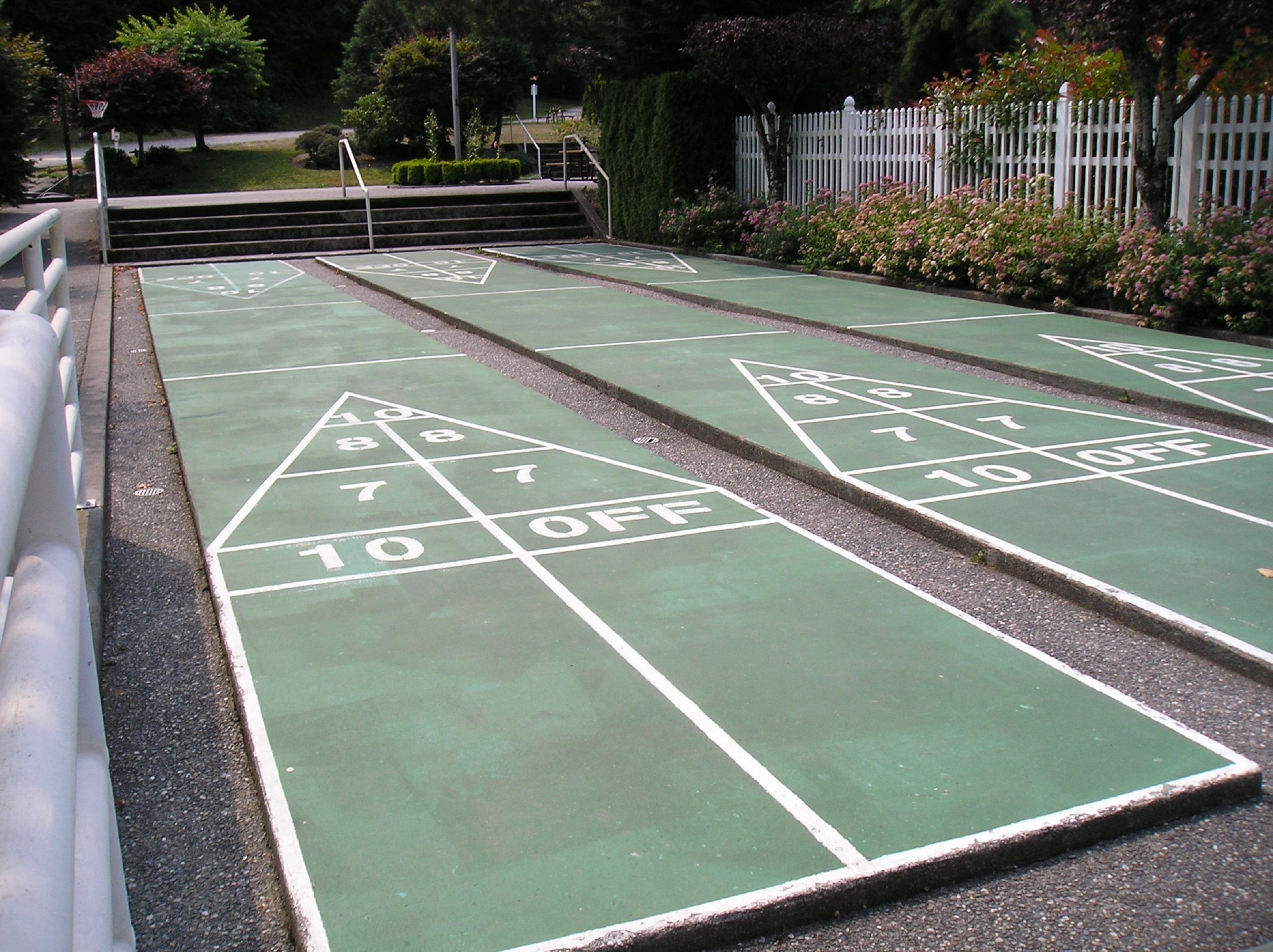 A shuffleboard court with numbered scoring areas and a white fence in the background.