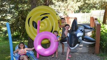 A playground with inflatable slides and rings, surrounded by trees and a wooden fence.