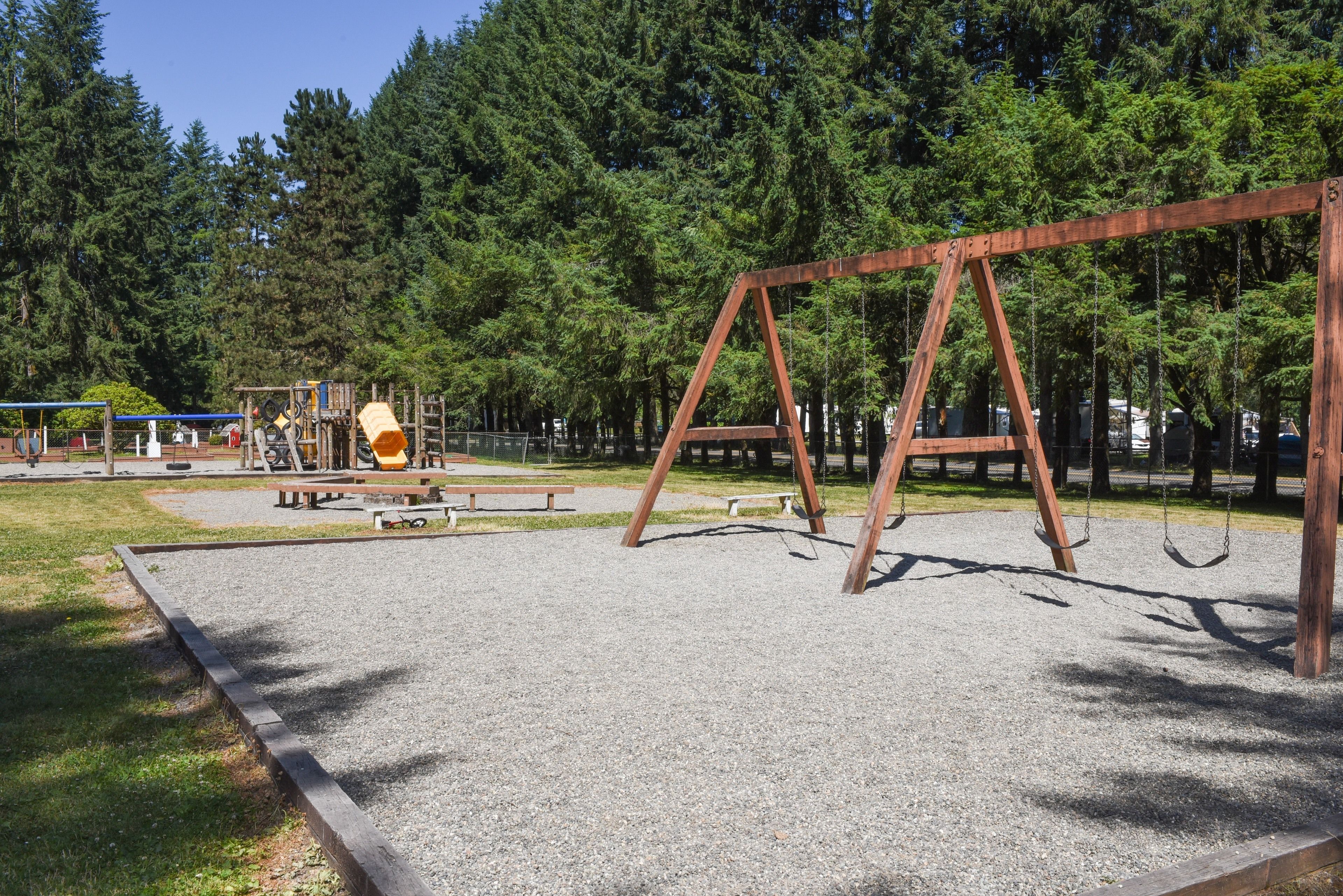A playground with swings and a slide, surrounded by trees.