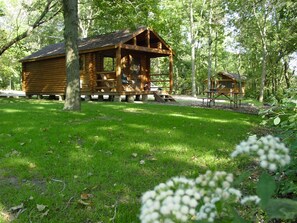Een houten chalet in rustieke stijl met een veranda, omringd door gras en bomen.