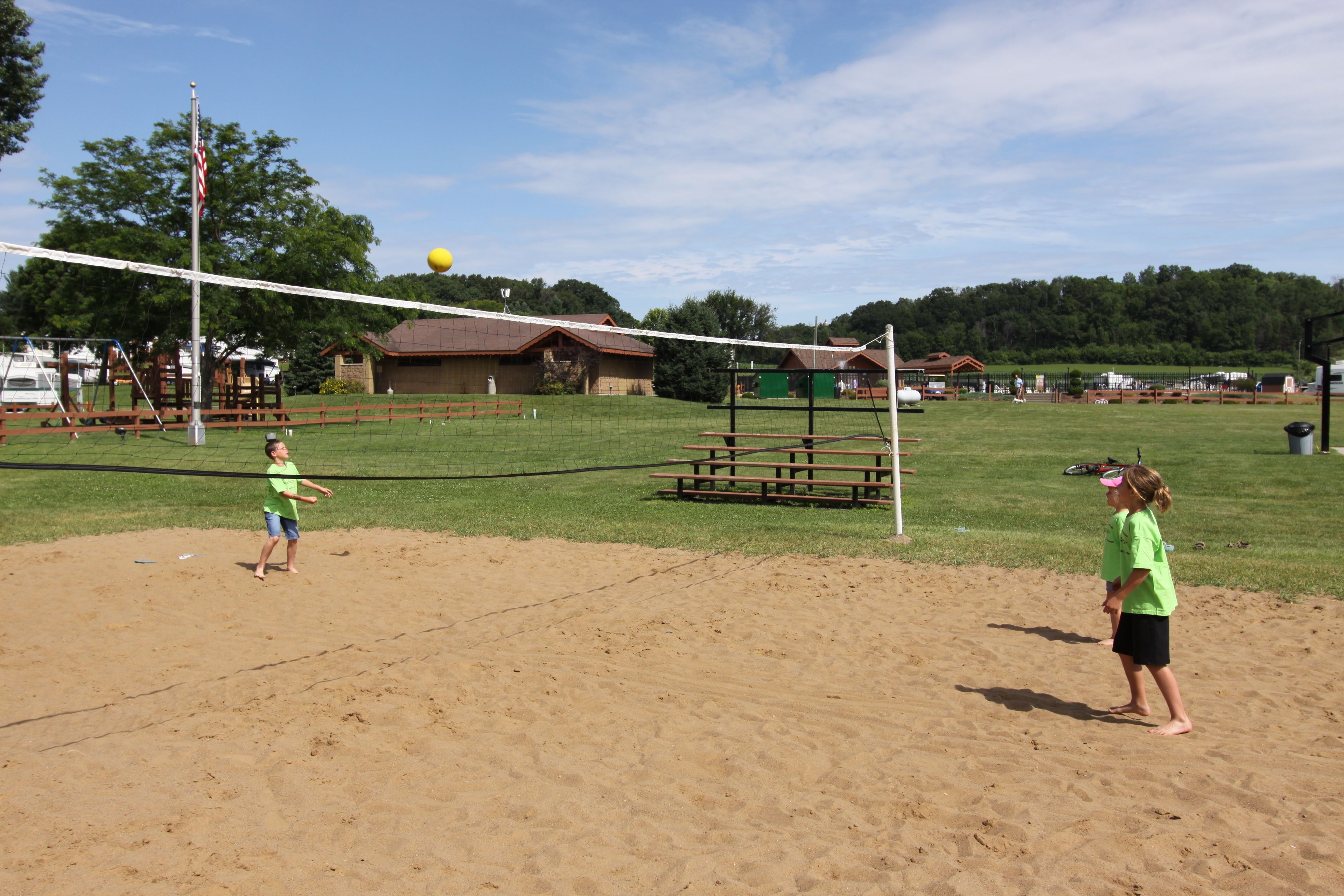 A volleyball court with a net, sand, and picnic tables.
