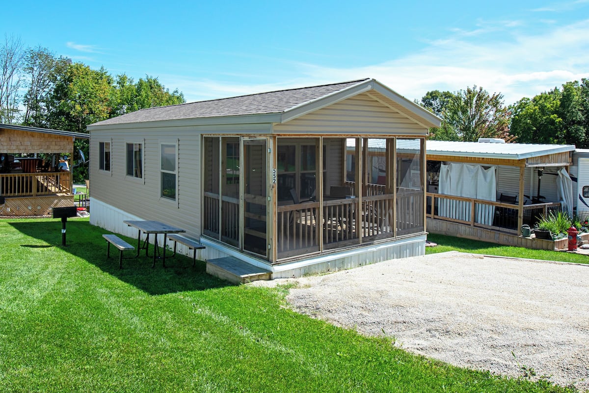 A mobile home with a screened porch, a small deck, and a gravel driveway.