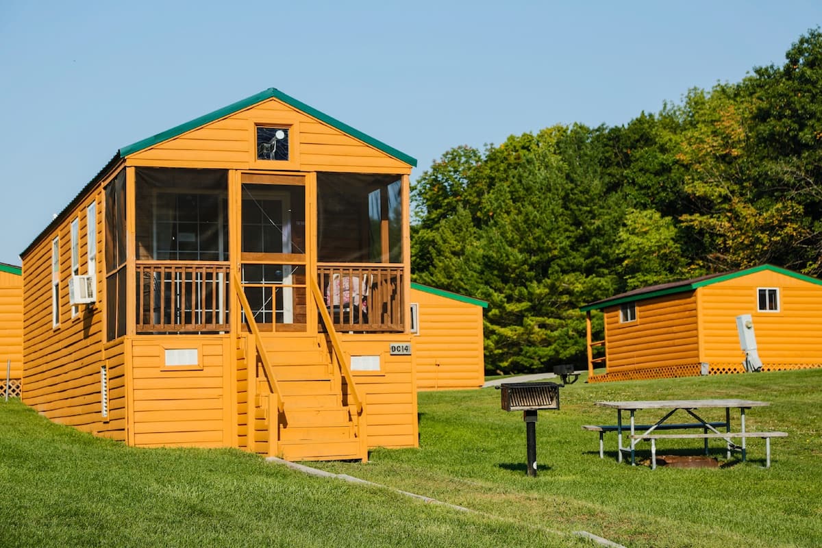 A yellow cabin with a balcony, a picnic table, and a green roof.
