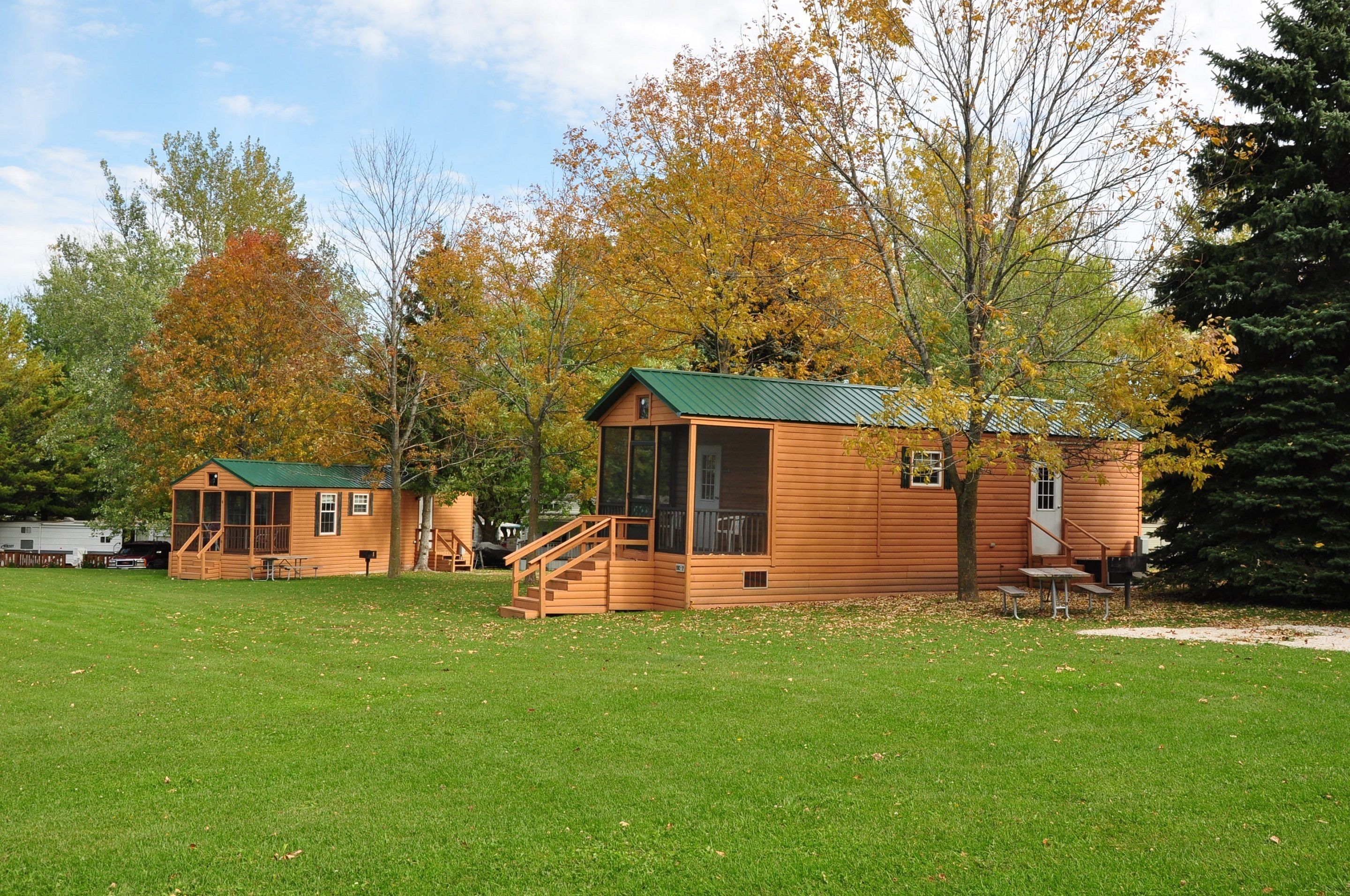 A wooden cabin with a green roof, a porch, and a staircase leading to the entrance.