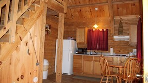 A wooden cabin interior with a kitchen, dining area, and a staircase. - Tranquil Timbers Camping Resort (Sturgeon Bay)