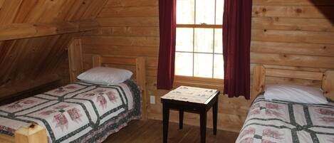 A cozy cabin room with two wooden beds, a small table, and a window with curtains.