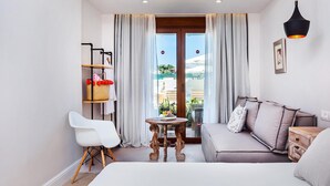 Quarto de hotel moderno com sofá, uma mesinha, uma cadeira e vista através de uma porta de vidro.
