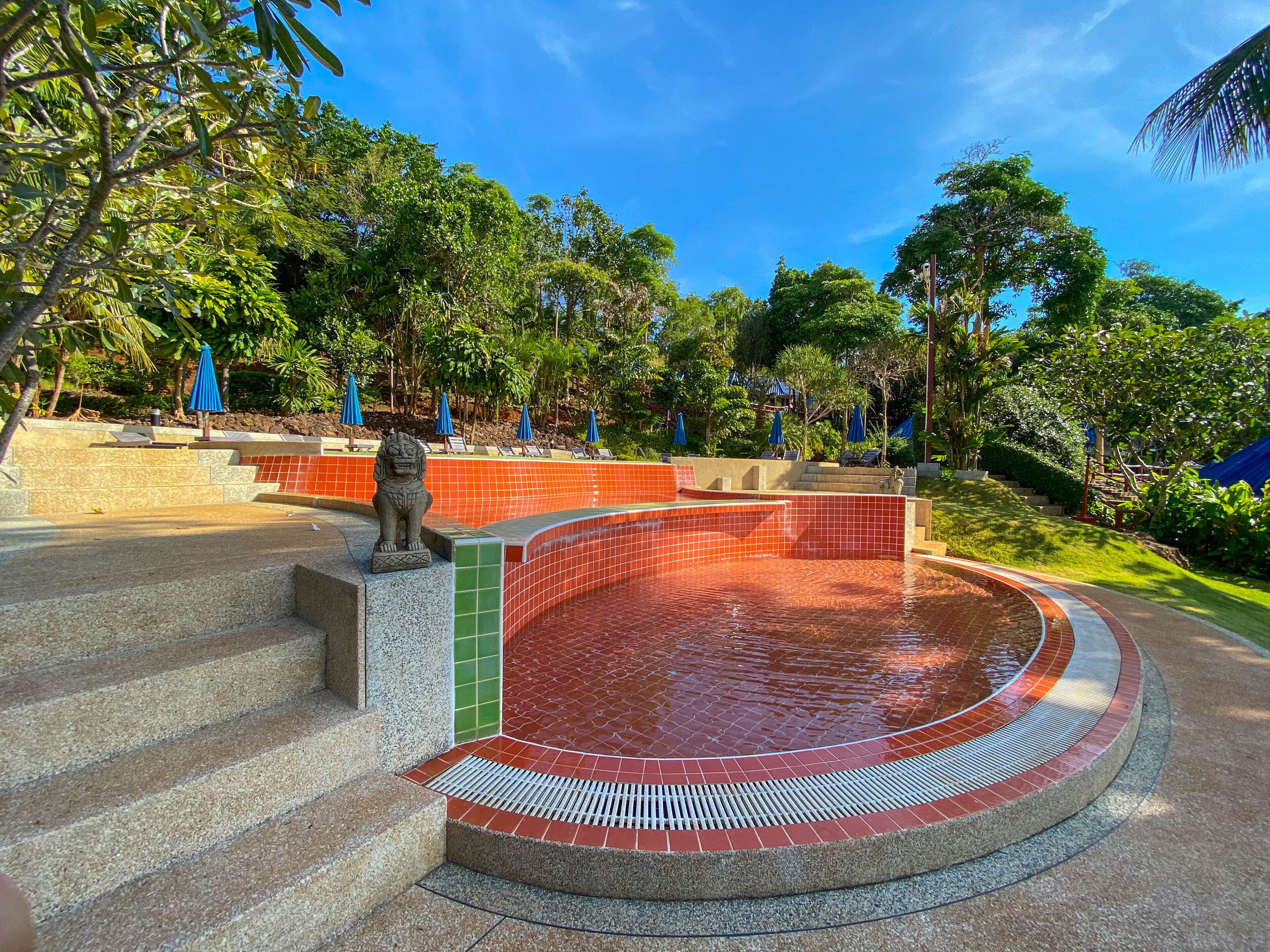 A swimming pool with red tiles, surrounded by steps and greenery.