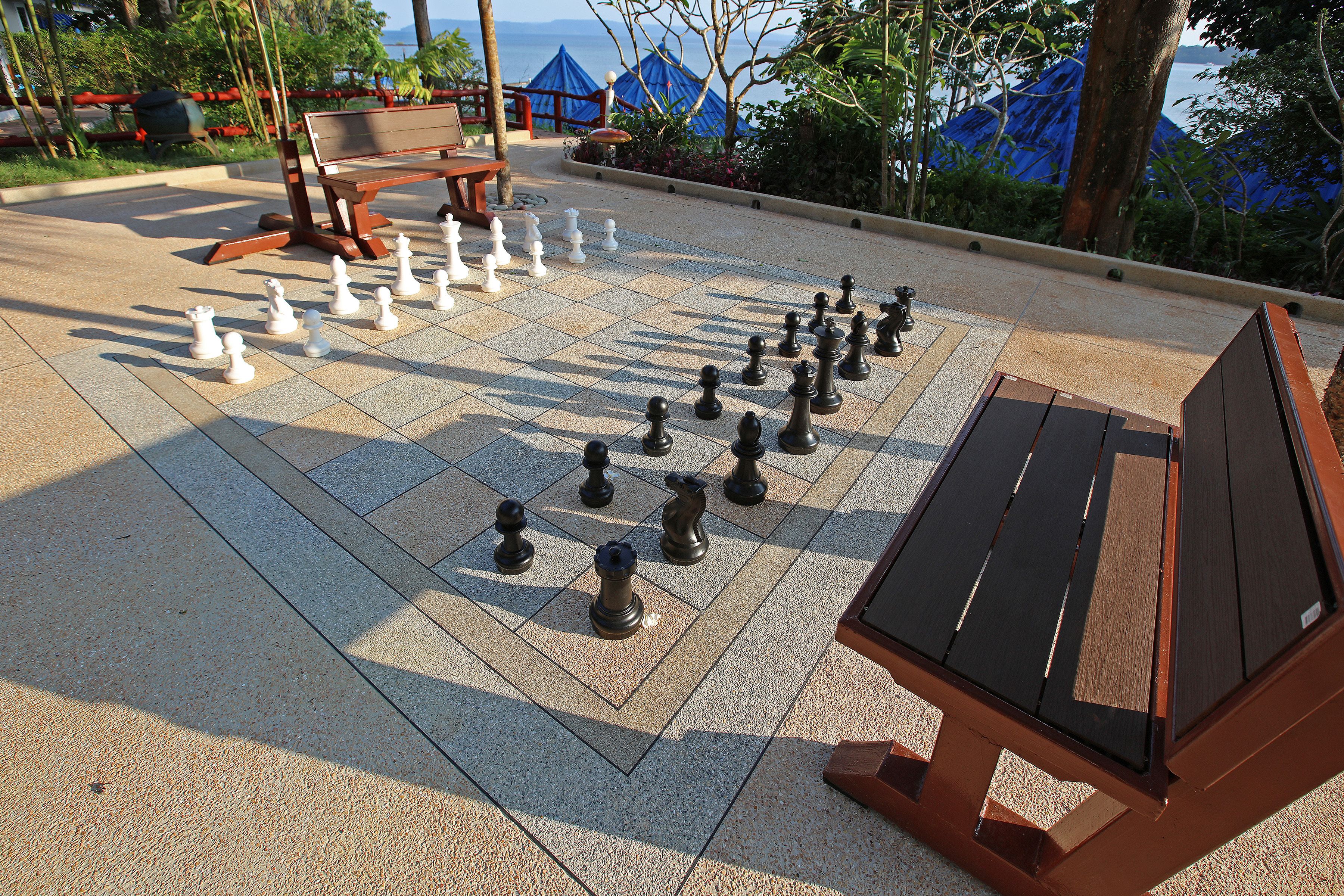 A chessboard set up on a paved area with a bench nearby.
