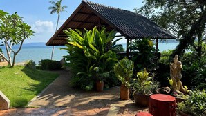 Un espace extérieur abrité, avec vue sur la mer, entouré de plantes tropicales et bordé d’un sentier en pierre.