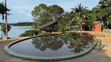 A swimming pool with a tiled edge, surrounded by a paved area with a gazebo and palm trees.