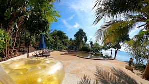 Un espace piscine agrémenté de chaises longues et de parasols, entouré d’une végétation tropicale et offrant une vue dégagée sur la mer.