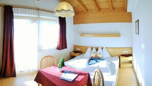A hotel room with a wooden ceiling, a bed with white bedding, a small table with a red tablecloth, a chair, and a potted plant. - Hotel-Restaurant Rosengarten (Zell am Ziller)