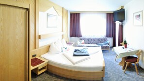 A hotel room with a bed, a sofa, a TV, and a small table with a chair. - Hotel-Restaurant Rosengarten (Zell am Ziller)