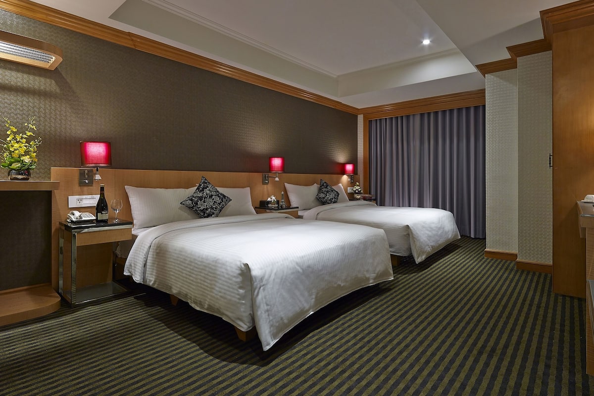 Ein Hotelzimmer mit zwei Betten, einem Schreibtisch, einem Sessel, einem Fernseher und einer Minibar.