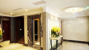 Eine Hotelhalle mit Marmorboden, einer Rezeption, einer Blumenkomposition und einem Aufzug.