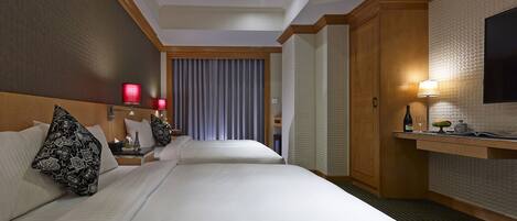Quarto de hotel com duas camas, uma escrivaninha com candeeiro, televisão e minibar.