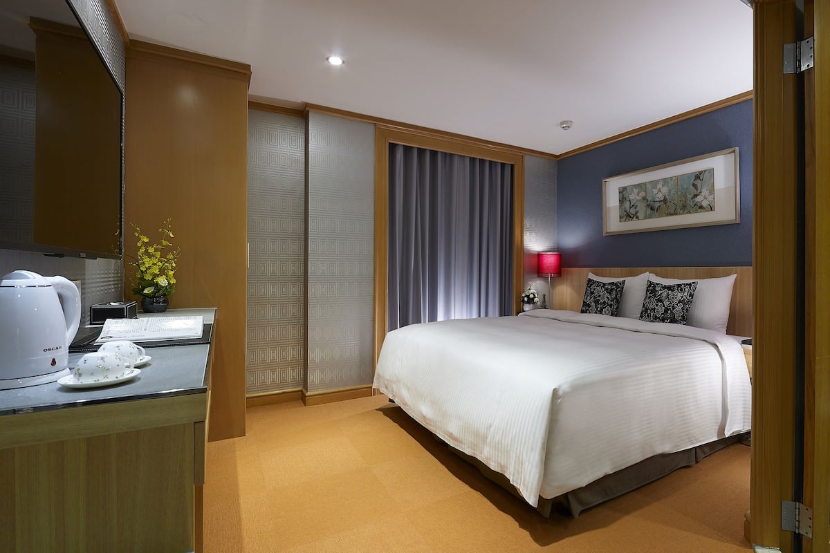 Ein Hotelzimmer mit einem Bett, einem Schreibtisch mit Wasserkocher, einer Lampe und einem Gemälde an der Wand.