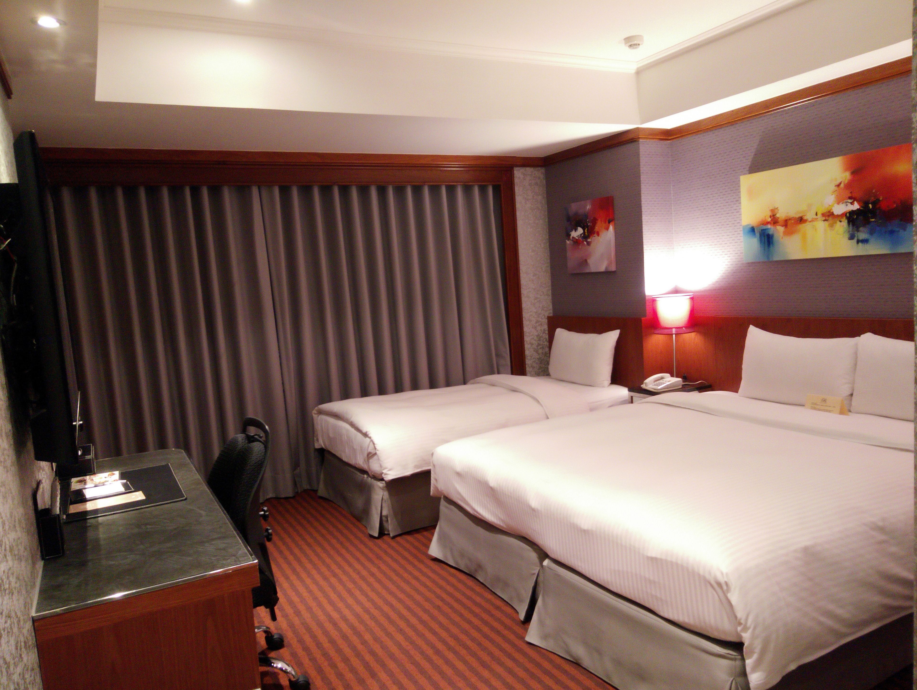 A hotel room with two beds, a desk, a chair, and a TV.