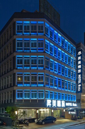 A multi-story hotel with illuminated blue window frames and a sign reading "Aisle Beauty Hotel."