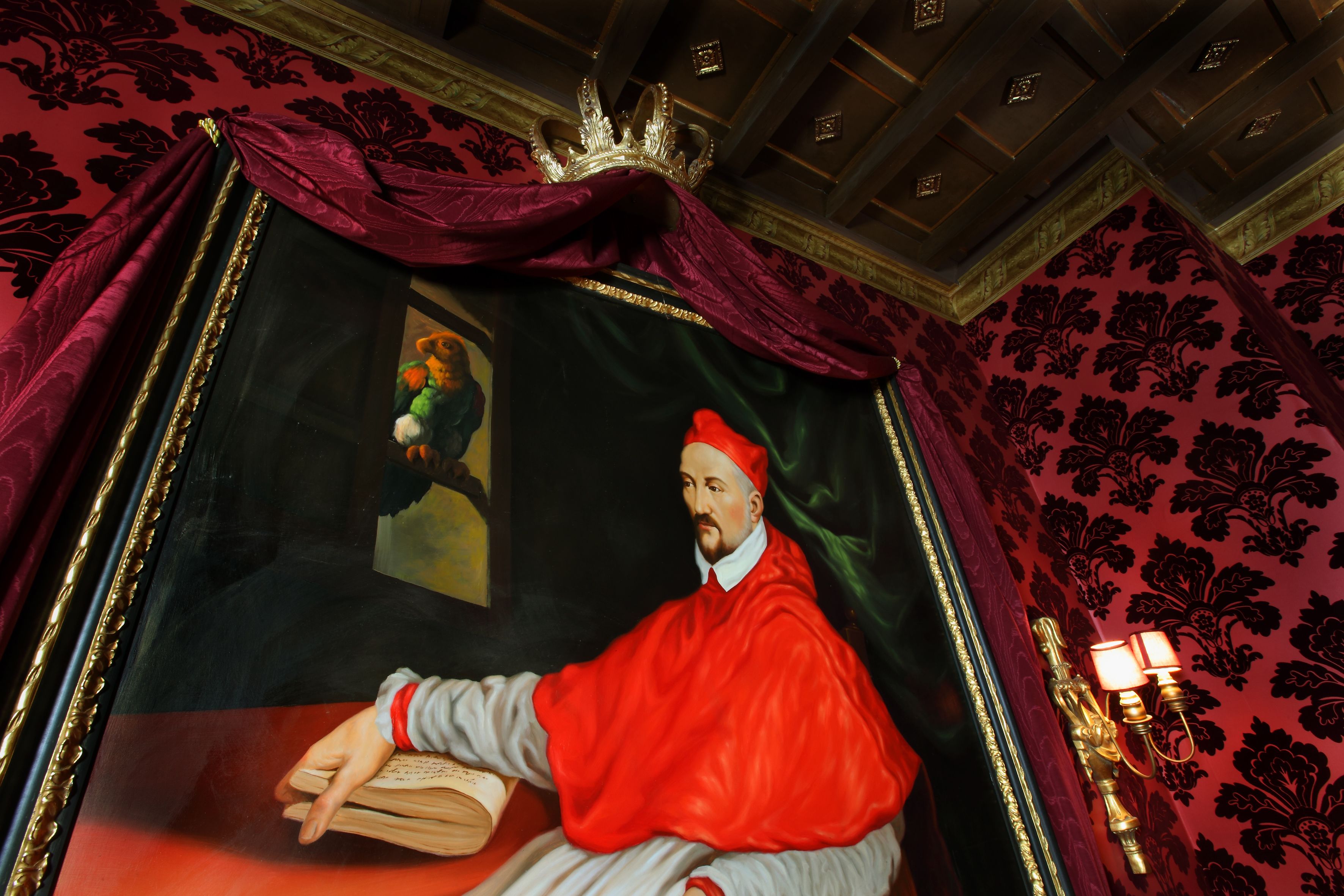 Une pièce décorée d’un grand tableau encadré représentant une figure vêtue de rouge, d’un lustre et d’un papier peint à motifs.