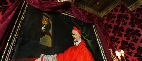 Une pièce décorée d’un grand tableau encadré représentant une figure vêtue de rouge, d’un lustre et d’un papier peint à motifs.
