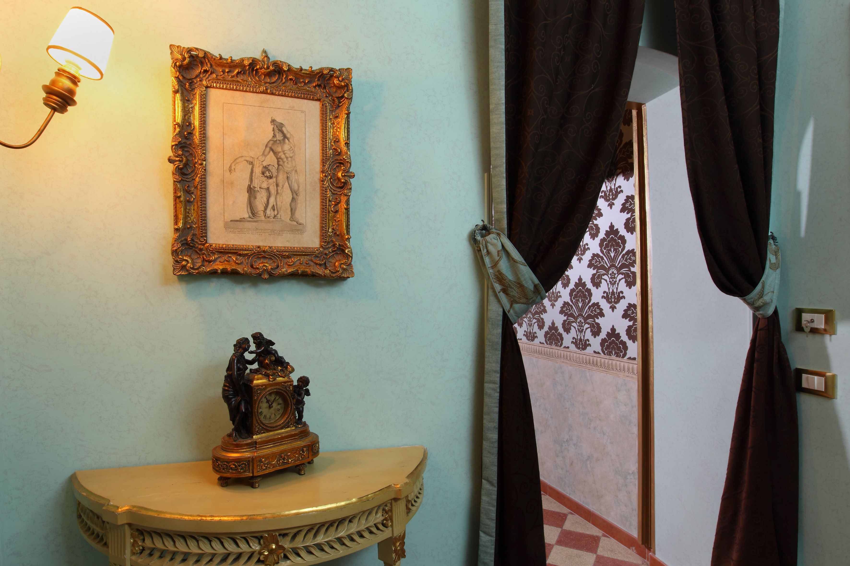 Une pièce avec un cadre photo accroché au mur, une petite table sur laquelle se trouve une horloge, et une porte ornée de rideaux à motifs.