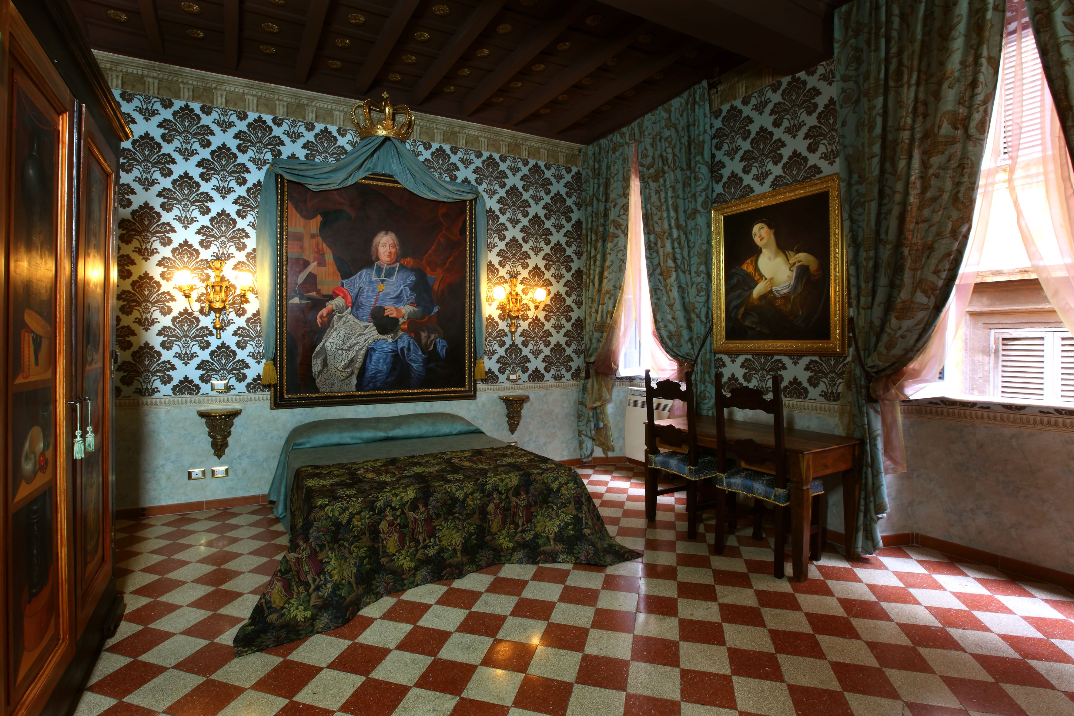 A room with a checkered floor, a bed with a patterned bedspread, a wooden chair, a wooden table, and two wall-mounted lamps.