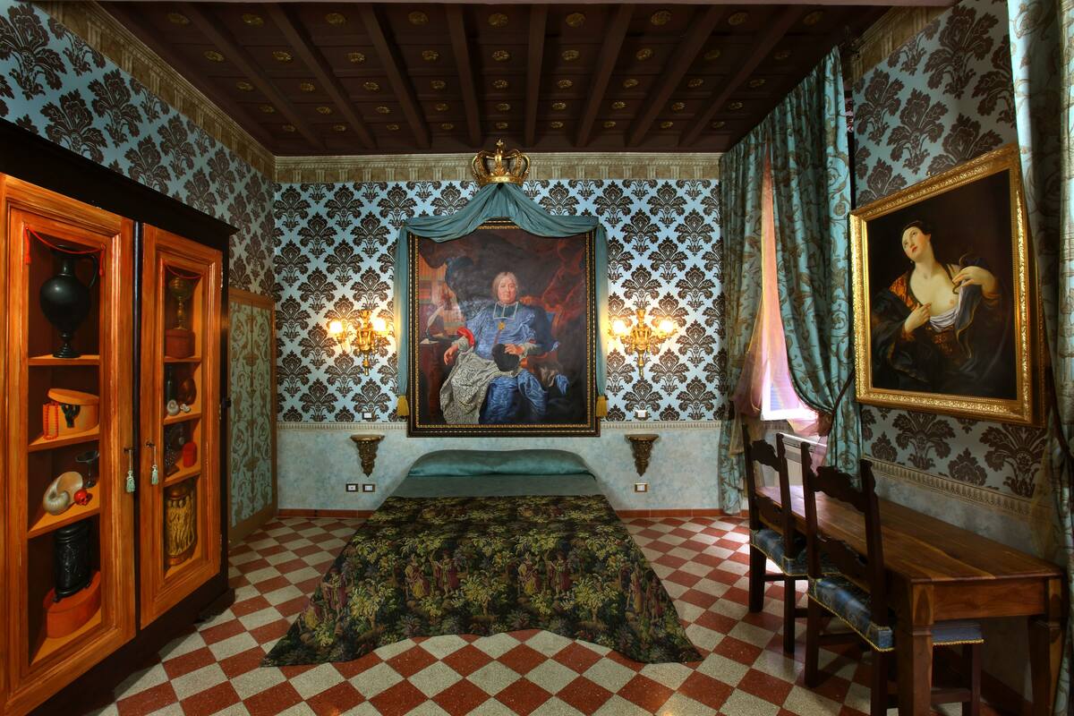 A room with a checkered floor, a bed with a patterned bedspread, a wooden cabinet with glass doors, and two wall-mounted lamps.