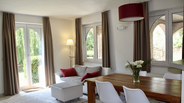 Ein moderner Essbereich mit einem Holztisch, weißen Stühlen, einer Couch mit roten Kissen und einer Blumenvase.