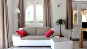Ein modernes Wohnzimmer mit einem weißen Sofa, roten Kissen, einem kleinen Tisch, einer Lampe und einer Topfpflanze.
