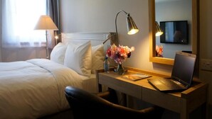 A hotel room with a bed, a desk with a laptop, a lamp, a vase with flowers, and a TV on the wall. - The Abergavenny Hotel  (Abergavenny)