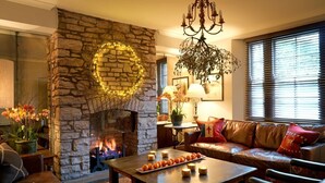 A cozy living room with a stone fireplace, leather sofa, and a coffee table with candles. - The Abergavenny Hotel  (Abergavenny)