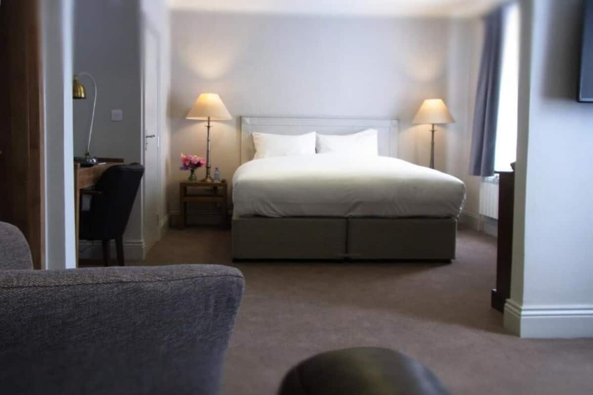Habitación de hotel con una cama, dos lámparas de noche, un escritorio con una silla y un televisor en la pared.