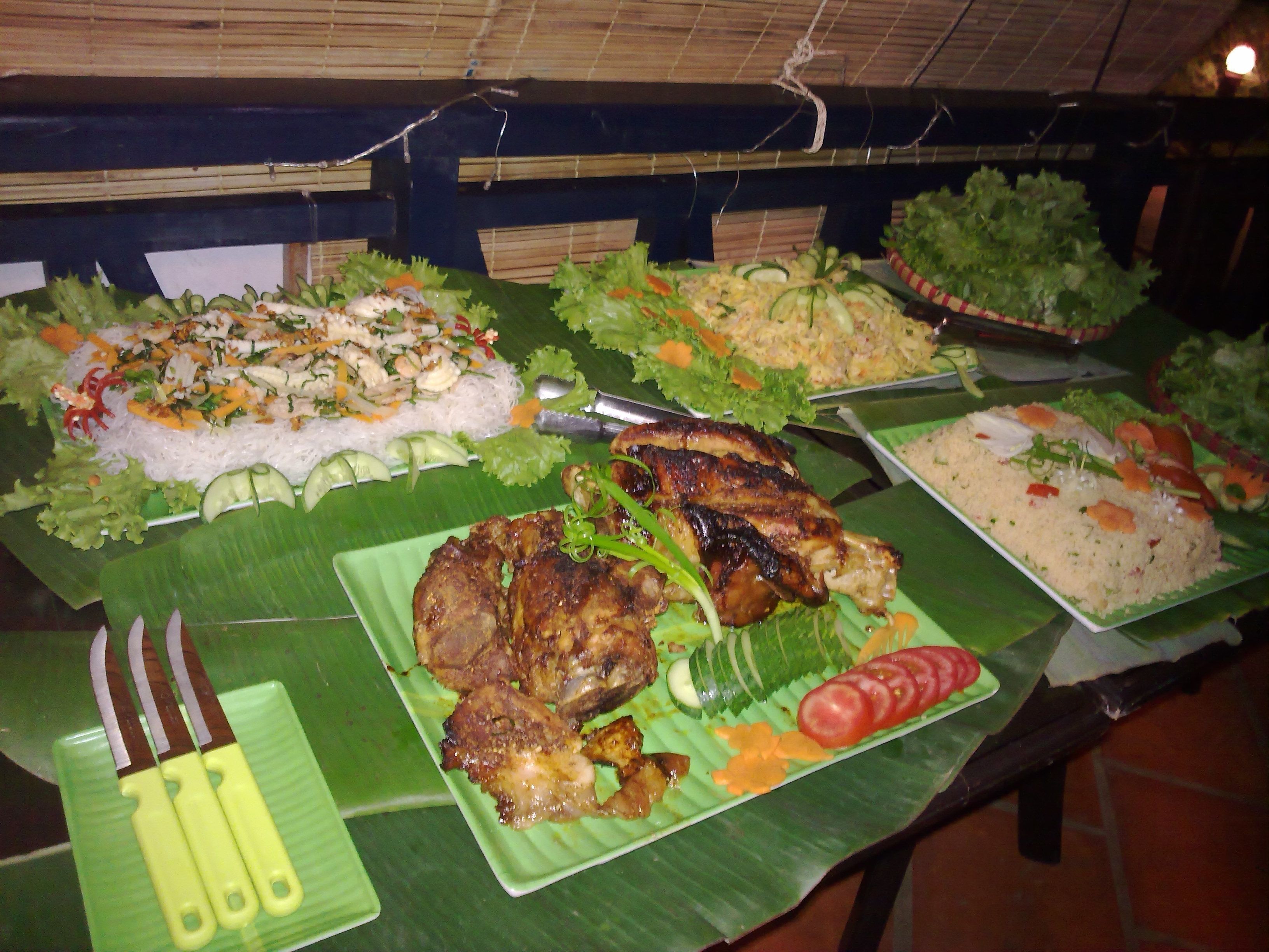 A buffet table with various dishes, including rice, vegetables, and grilled meat, set on a green tablecloth.