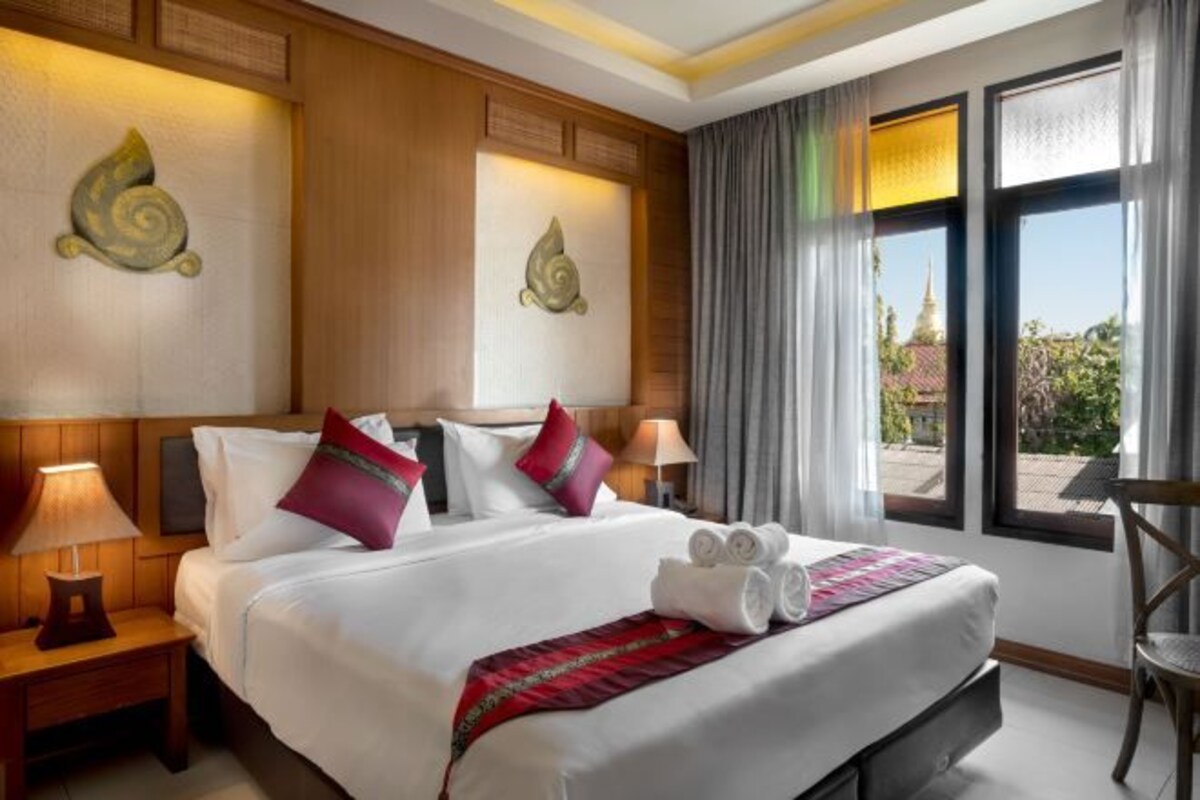A hotel room with a large bed, two bedside lamps, a view of a temple through the window, and a chair by the window.