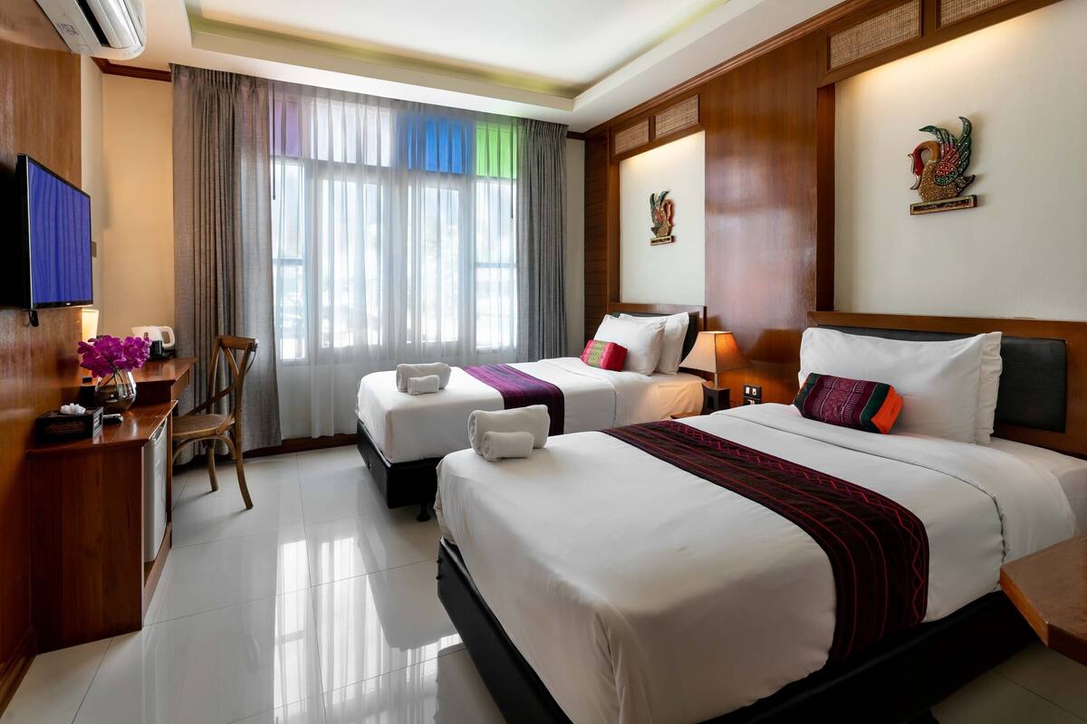 A hotel room with two beds, a desk with a computer, a TV, and a window with curtains.