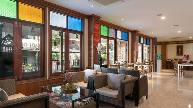 A spacious lobby with wicker furniture, large windows with colorful glass panels, and a dining area in the background. - Lee Chiang Hotel (Chiang Mai)