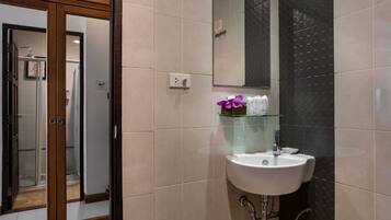 A bathroom with a white sink, a glass shelf with toiletries, a mirror, and a shower area visible through a glass door.
