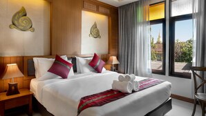 A hotel room with a large bed, two bedside lamps, a view of a temple through the window, and a wooden headboard. - Lee Chiang Hotel (Chiang Mai)