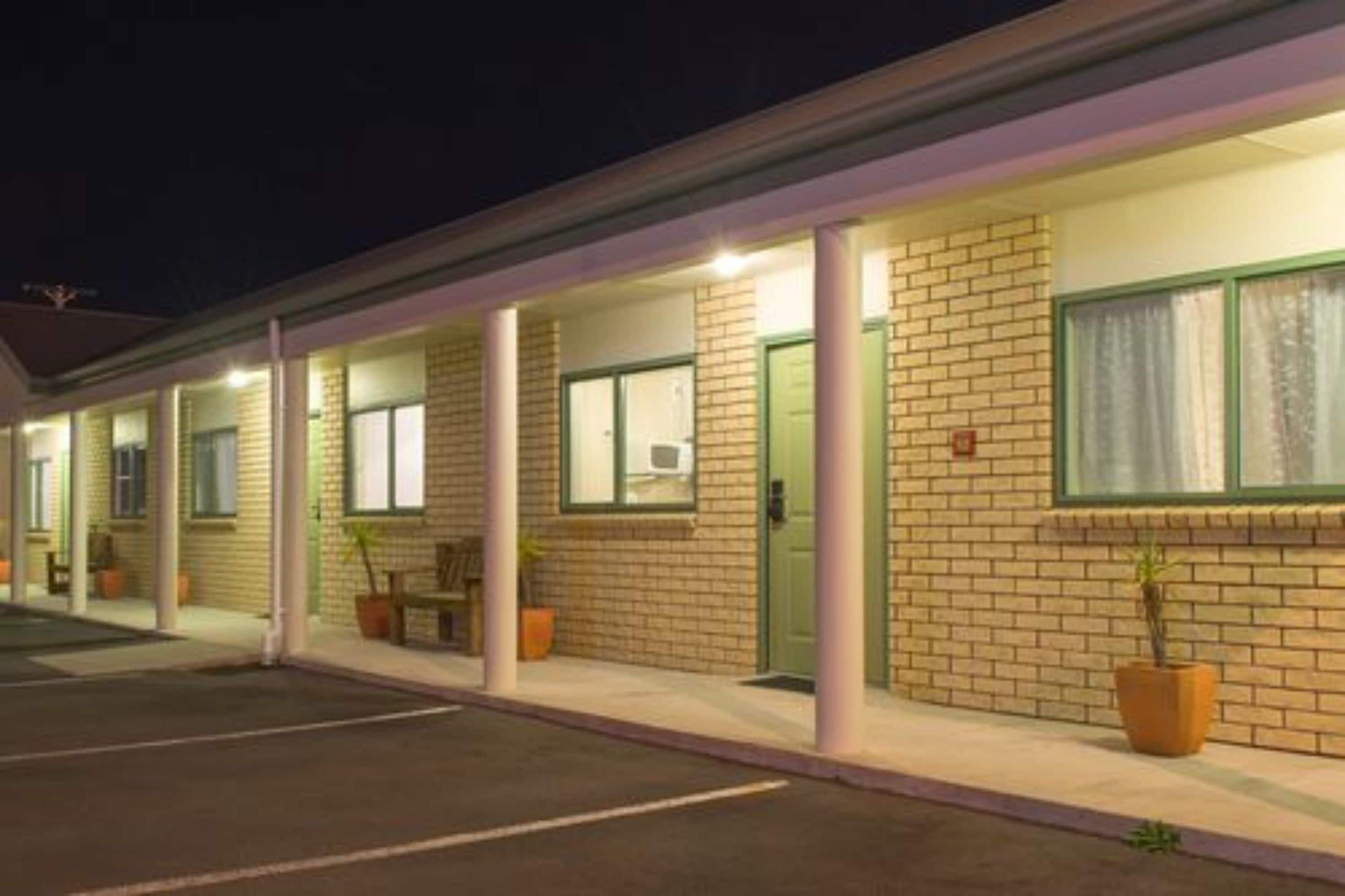 Un motel con fachada de ladrillo, habitaciones individuales con ventanas y un área de estacionamiento techada.