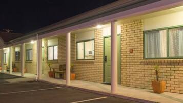 Un motel con fachada de ladrillo, habitaciones individuales con ventanas y un área de estacionamiento techada.