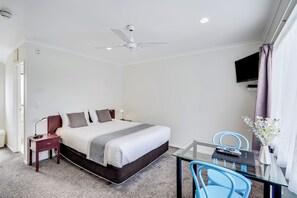 A hotel room with a bed, bedside table, lamp, TV, and a small table with chairs. - Hamilton Settlers Motor Lodge (Hamilton)