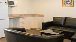 A compact living space with a black leather sofa and armchair, a small coffee table, a kitchenette with a microwave, and a framed picture on the wall. - Hamilton Settlers Motor Lodge (Hamilton)