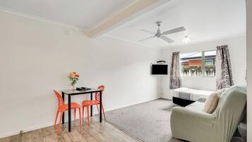 A room with a dining table, chairs, a sofa, a ceiling fan, a TV, and a window with curtains.