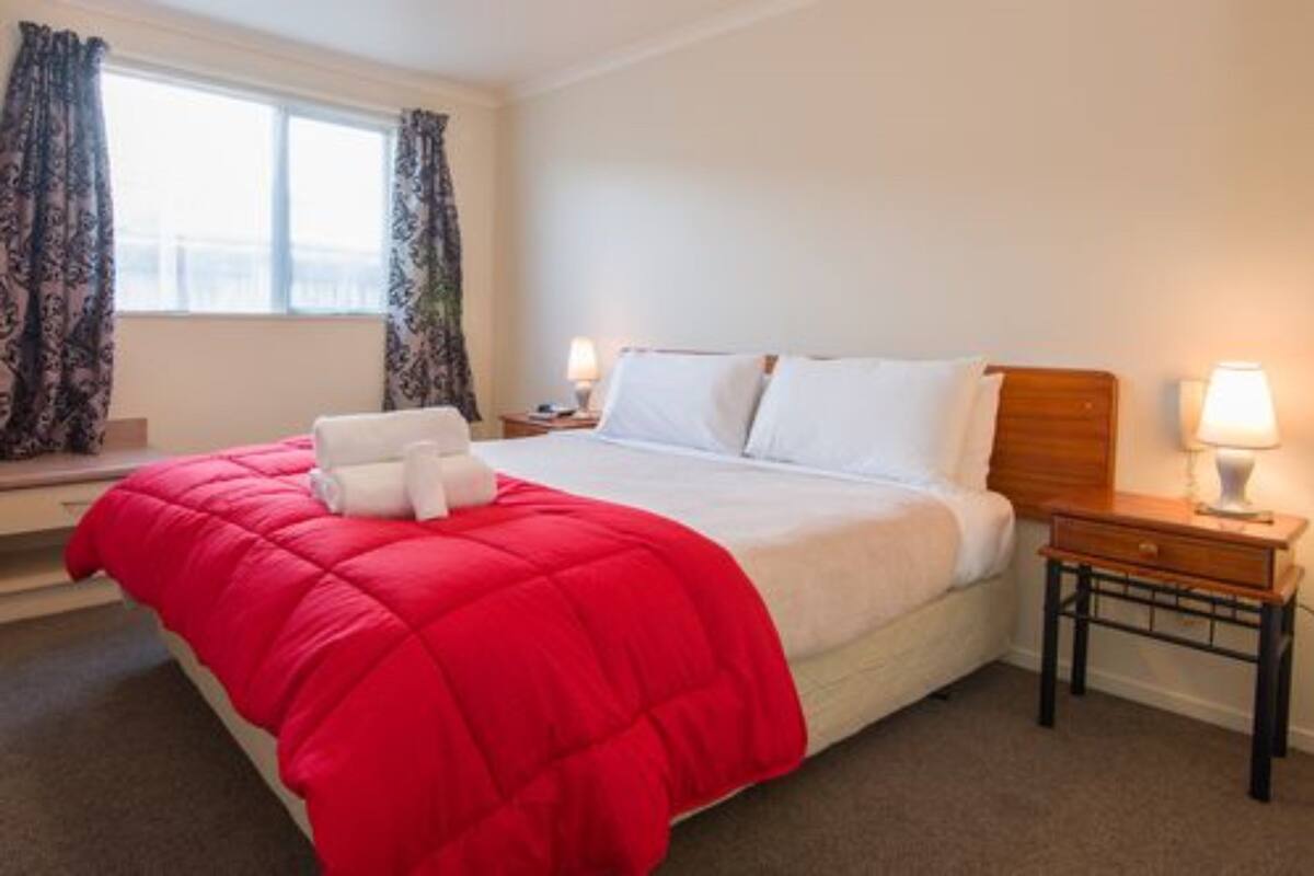 A hotel room with a bed, a nightstand, a lamp, and a window with curtains.