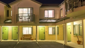 A two-story building with green doors, a balcony, and a bench outside. - Hamilton Settlers Motor Lodge (Hamilton)